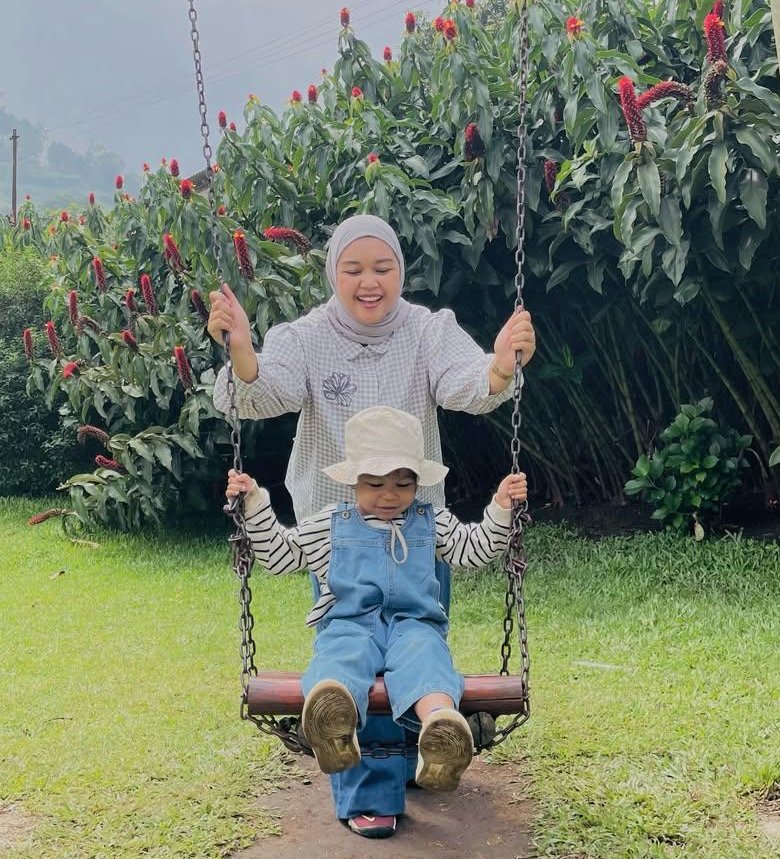 Original photo: a mother in a hijab and a toddler in a sun hat on a wooden swing in a garden with red flowers